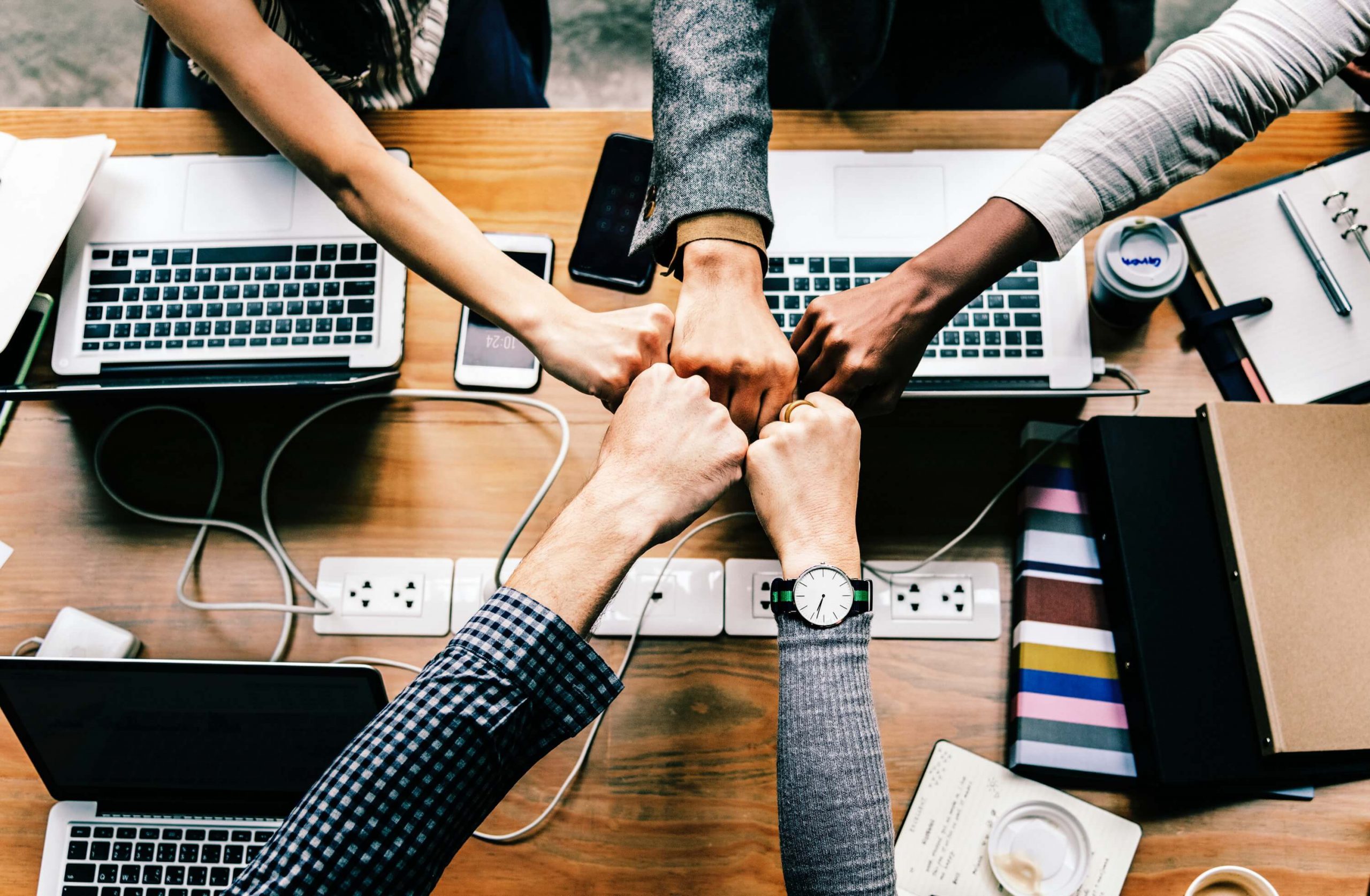 Five men and women reach out their hands from out of frame for a group fist bump. 